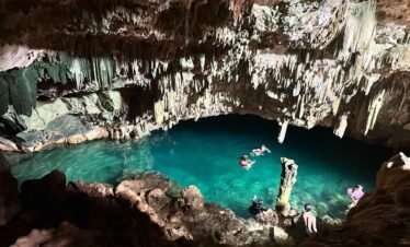 Swimmers in the crystal-clear water of Rangko Cave, surrounded by stalactites and rocks inside the underground cave.Rangko Cave tour