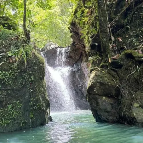 Hidden waterfall cascading between mossy rocks at Cunca Lolos, Flores
