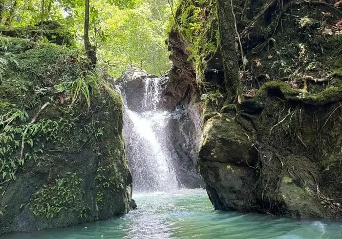 Hidden waterfall cascading between mossy rocks at Cunca Lolos, Flores