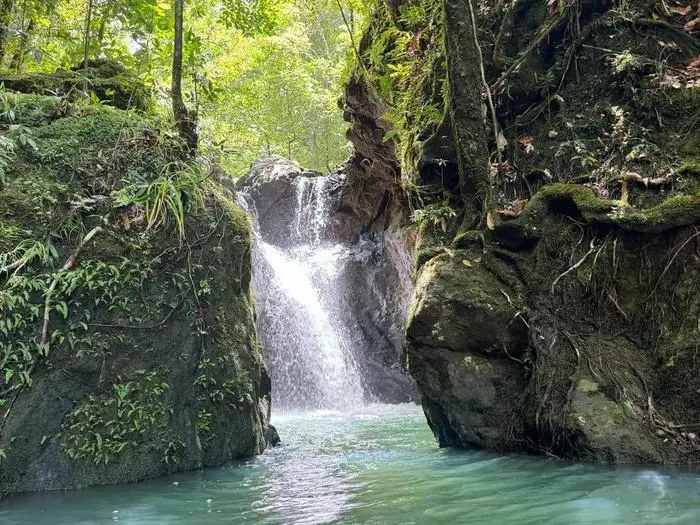 Hidden waterfall cascading between mossy rocks at Cunca Lolos, Flores