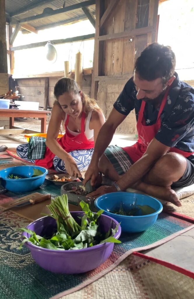 A group of people smiling and enjoying a homemade meal together in a village setting.