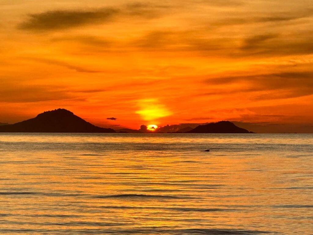 Labuan Bajo snorkeling trip ,Sunset over Labuan Bajo harbor with fishing boats bobbing in the ocean, vibrant and scenic.