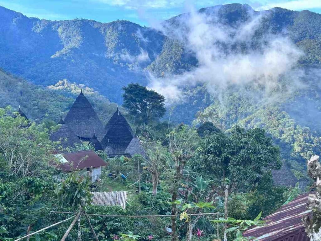 Visitors exploring Waerebo Village in Flores, Indonesia, with traditional cone-shaped Mbaru Niang houses in the highlands.