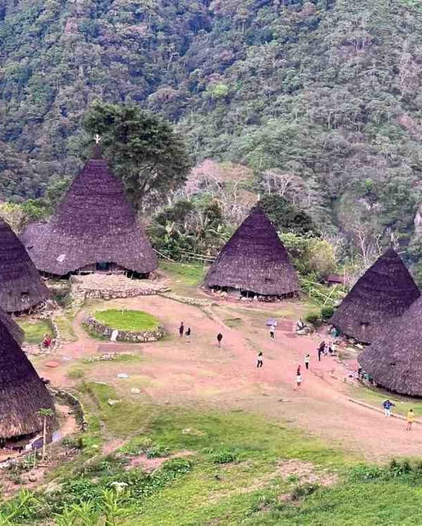 Aerial view of Waerebo Village in Flores Highlands with traditional Mbaru Niang houses surrounded by lush green mountains.