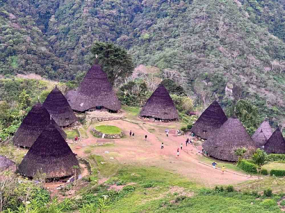Aerial view of Waerebo Village in Flores Highlands with traditional Mbaru Niang houses surrounded by lush green mountains.