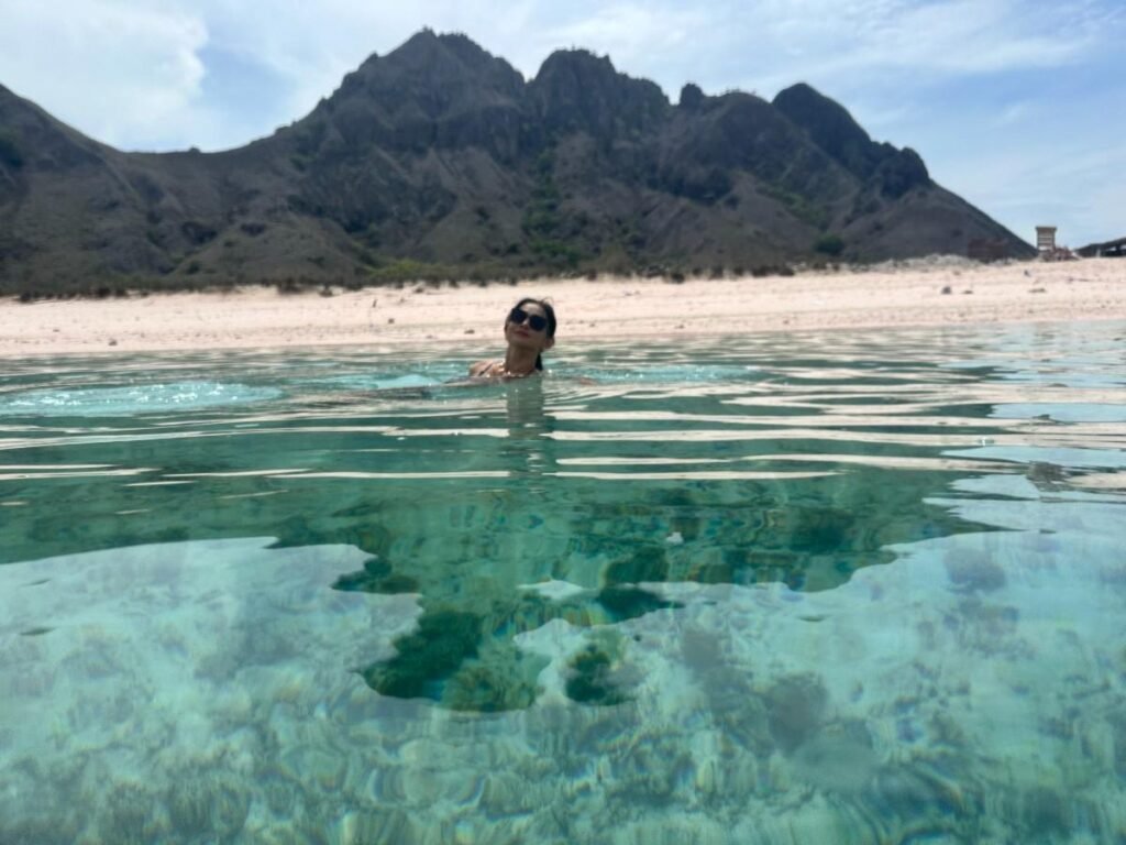 Woman swimming in clear turquoise water with mountains in the background.