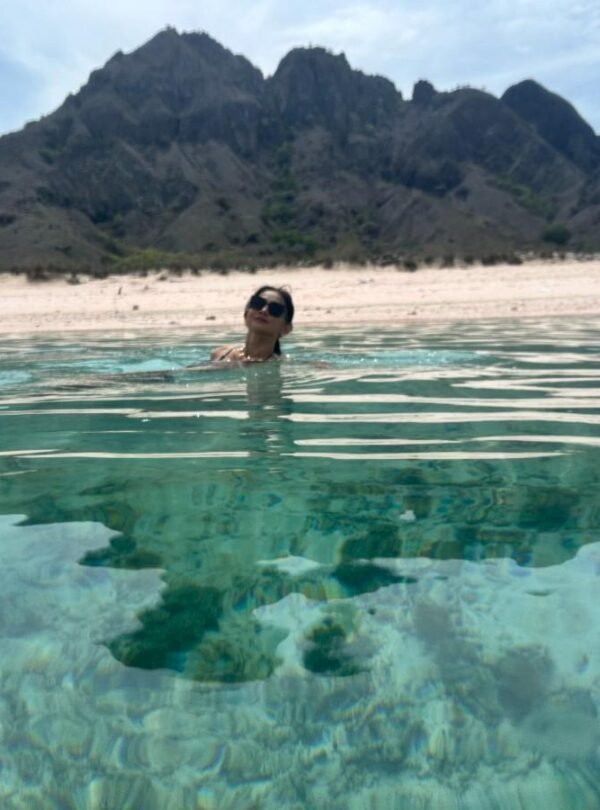 Woman swimming in clear turquoise water with mountains in the background.