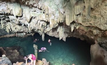 People swimming in Rangko Cave and relaxing in a natural pool inside a large cave with stalactites.