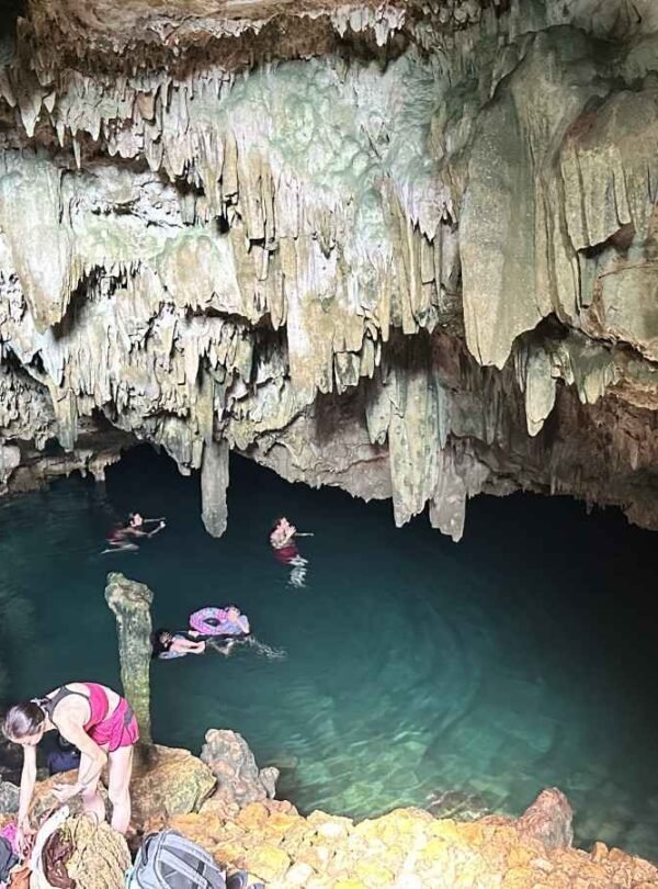 People swimming in Rangko Cave and relaxing in a natural pool inside a large cave with stalactites.