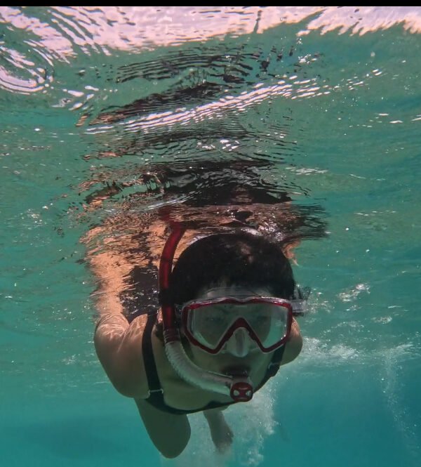Person snorkeling underwater with goggles and snorkel, surrounded by blue water and marine life.