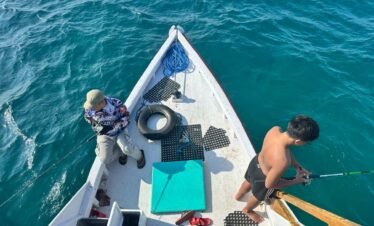 Two men fishing from the front of a traditional boat in clear blue Flores Sea