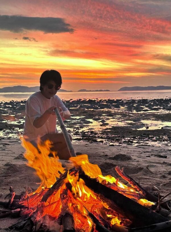 Person sitting beside a bonfire on Rangko beach during sunset ,Rangko Village Sunset Tour