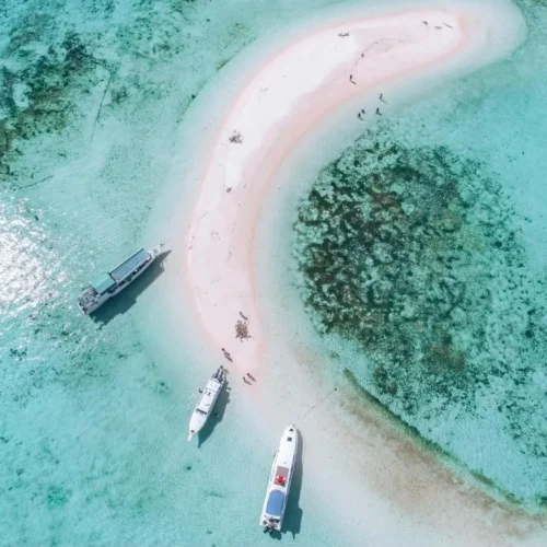 Private speedboats anchored beside a white sandbar in the turquoise waters of Komodo