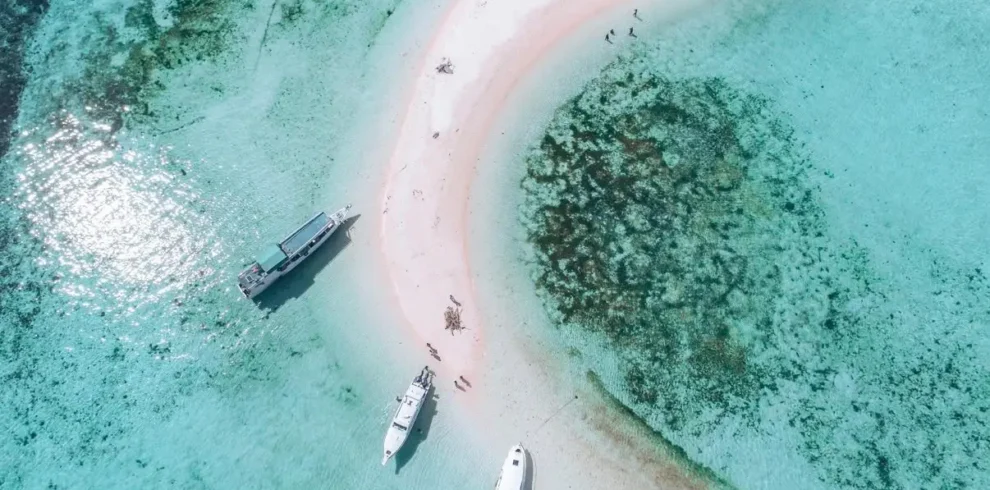 Private speedboats anchored beside a white sandbar in the turquoise waters of Komodo