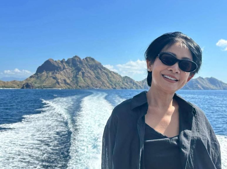 Chef Ina smiling on a boat in Labuan Bajo with Komodo Island in the background